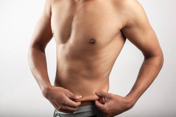 An asian young man pulling skin on the abdomen, showing the body fat in the abdominal area.